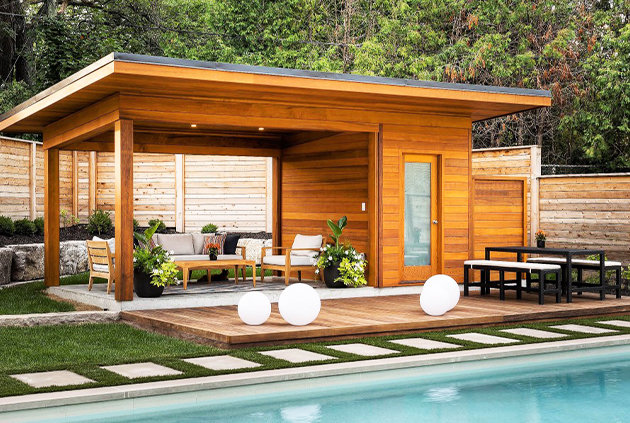 Poolside cabana with outdoor furniture accessories and wooden fence surrounding the perimeter. 